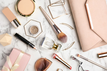 Flat lay composition with different luxury makeup products and accessories on white marble table
