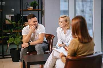 smiling caucasian couple sit in own office of family psychologist, happy sit having conversation with therapist, they want to solve problems with emotional side of relationship. people, family concept