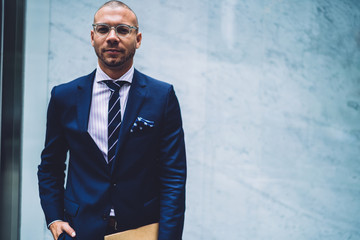 Half length portrait of male adult student posing at urban setting with copy space promotional background for text advertising, confident man in classic glasses and formal suit at publicity area