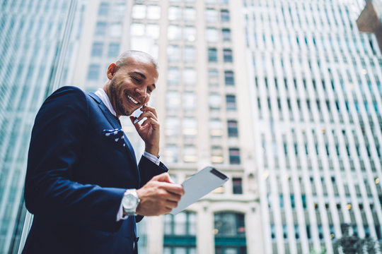 Below view of Caucasian educator 30s reading information about banking account while making international cellphone conversation, happy businessman phoning for consultancy about roaming service