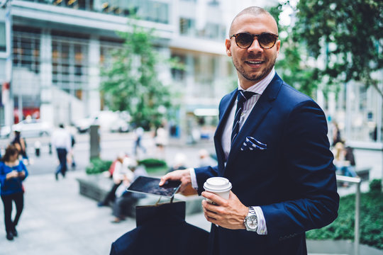 Businessman in suit carrying coffee cup and tablet while looking away though sunglasses