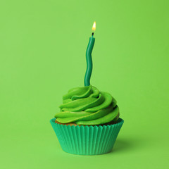 Delicious birthday cupcake with burning candle on green background