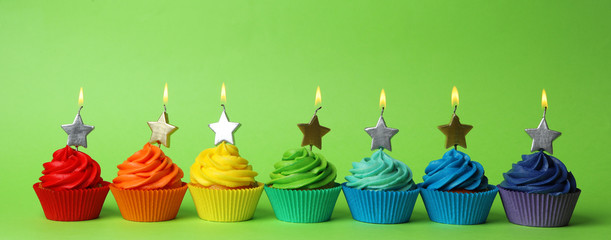 Delicious birthday cupcakes with burning candles on green background