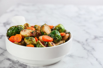 Delicious roasted Brussels sprouts with carrot on white marble table, closeup