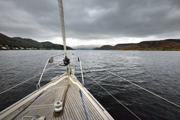 Sloop rigged modern yacht with wooden teak deck sailing on a cloudy day. A view from the deck to...