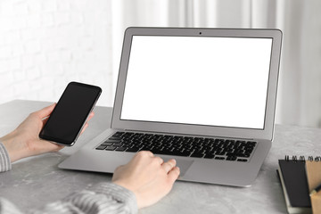 Woman using laptop and smartphone at desk in office, closeup. Space for design