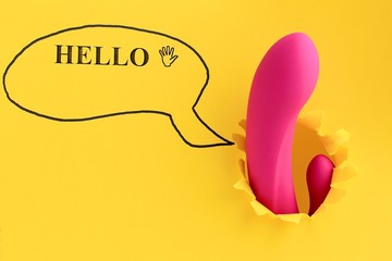 Sex toy for adult, dildo vibrator looking through a hole in the yellow paper with text hello. Funny...