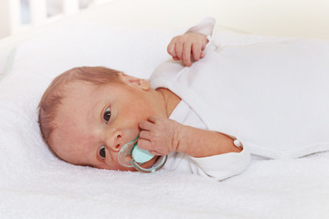 Portrait of little newborn baby boy laying and holding pacifier with hand