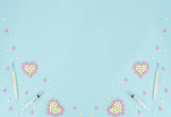 Hearts made of pink and yellow pills, thermometer, syringe on light blue background. Seasonal diseases. Medicine concept. Flat lay style with copy space, top view.