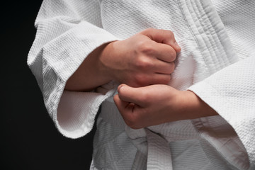 hands closeup - teenager dressed in martial arts clothing posing on a dark gray background, a sports concept