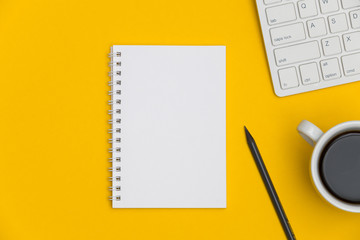Workplace with blank notepad, coffee cup, keyboard and supplies on bright yellow desk background. Top view. Minimal flat lay