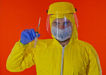 Man in yellow chemical protection suit and face protective mask coronavirus. Without glasses. Protective helmet. Hands in blue gloves. Yellow vaccine syringe.