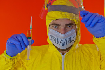 Man in yellow chemical protection suit and face protective mask coronavirus. Without glasses. Protective helmet. Hands in blue gloves. Yellow vaccine syringe.