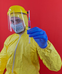 Man in yellow chemical protection suit and face protective mask coronavirus. Without glasses. Protective helmet. Hands in blue gloves. Syringe with red liquid.