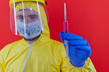 Man in yellow chemical protection suit and face protective mask coronavirus. Without glasses. Protective helmet. Hands in blue gloves. Syringe with red liquid.