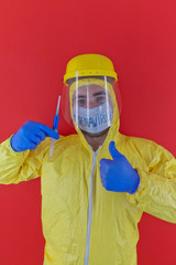 Man in yellow chemical protection suit and face protective mask coronavirus. Without glasses. Protective helmet. Hands in blue gloves. Blue vaccine syringe. Thumb up.