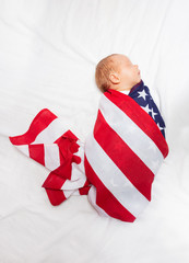 Portrait of little baby infant boy wrapped in USA flag laying on the bed sheet