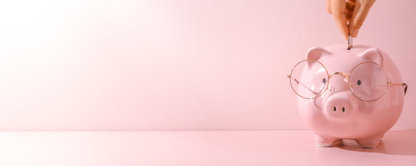 Female finger putting a coin into piggy bank