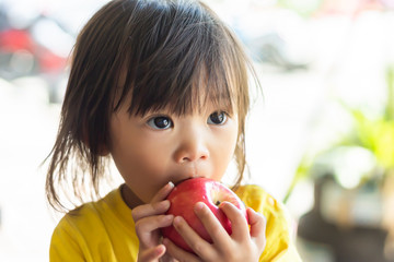 Portrait​ image​ of​ 1-2​ yeas​ old​ of​ baby.​ Happy​ Asian child girl eating and biting an red apple. Enjoy eating moment. Healthy food and kid concept.​ Vintage​ style.