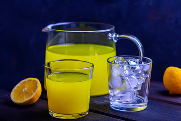 Homemade refreshing citrus lemonade in pitcher and in glass, and glass with ice cubes on a wooden background. Fresh orange juice. The concept of organic drink and fresh vitamins. Copy space for text