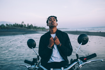 Motorcyclist adjusting bomber jacket on seashore