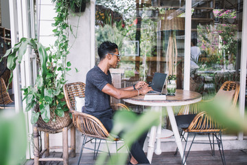 Concentrated freelancer typing on laptop in summer cafe