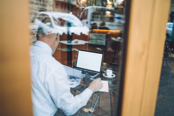 Grey haired man using laptop taking notes at cafe
