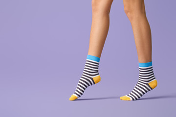Legs of young woman in striped socks on color background