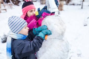 Happy kids making a snowman together in winter park after snowfall