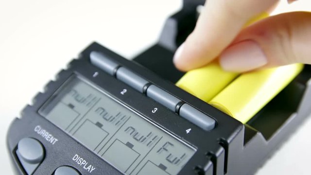 Close up of installing a battery into a charger. Batteries are charged in a charger. AA and AAA battery charger background close-up. Green technology for environment protection