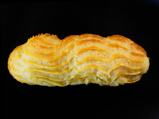 One eclair on a black background. Cake close-up, top view.