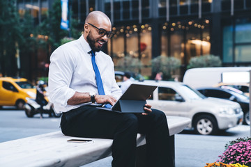 Black excited manager typing on tablet on street