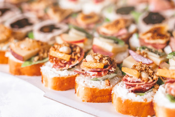 Crostini with meat, fruits, vegetables and cheese close up on table.