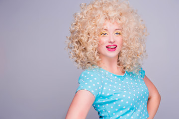 Fototapeta premium Beautiful retro-style blonde girl with voluminous curly hairstyle, in a blue polka-dot blouse on a gray background, smiles and looks at the camera