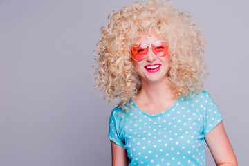 Beautiful retro-style blonde girl with voluminous curly hairstyle, in a blue polka-dot blouse and pink glasses on a gray background