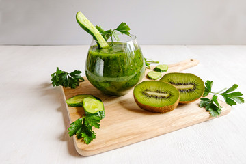 On a wooden table is a glass glass with green homemade smoothies. Next to the Ingredients-kiwi, cucumbers, parsley. Vegetarianism, diet, detoxification-a healthy lifestyle. Copy space