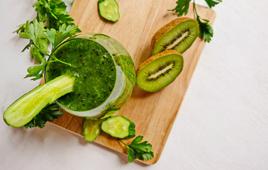 On a wooden table is a glass glass with green homemade smoothies. Next to the Ingredients-kiwi, cucumbers, parsley. Vegetarianism, diet, detoxification-a healthy lifestyle. Copy space