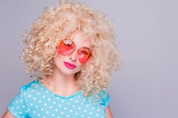 Beautiful retro-style blonde girl with voluminous curly hairstyle, in a blue polka-dot blouse and pink glasses on a gray background