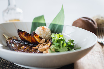 Asian cuisine, baked eggplant with nuts and rice in a deep plate on a table in a restaurant.