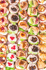 Top view of crostini with meat, fruits, vegetables and cheese close up on table.