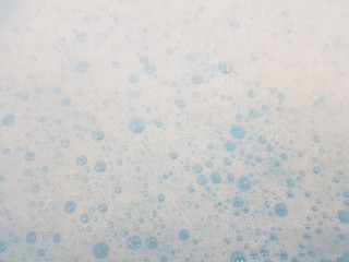 White foam with bubbles popping in blue water closeup.