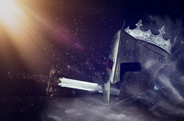 photo of crown over king knight helmet armor and sword over dark background. Medieval period concept