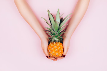 Hands with pineapple on stylish pink background.