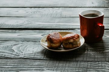 dark wooden background on it is a texture. A cup of black coffee and 2 donuts from homemade pastries with a filling inside