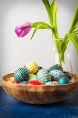 Easter bunny in basket with colorful eggs and tulips on wooden table. Easter holiday decorations , Easter concept background.