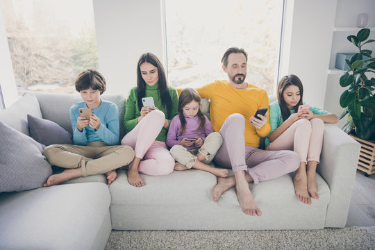 Portrait of nice attractive bare foot big full focused family pre-teen kids sitting on divan using 5g app internet online wi-fi connection browsing surfing at light white interior style house