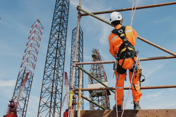 worker on high on scaffolding wearing full body safety harness on oil rig drilling brage stand structure background.