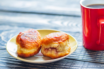 dark wooden background on it is a texture. A cup of black coffee and 2 donuts from homemade pastries with a filling inside