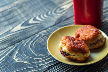 dark wooden background on it is a texture. A cup of black coffee and 2 donuts from homemade pastries with a filling inside