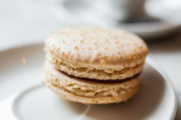 Fototapeta na wymiar A close up photo of a macaron with salted caramel on a white saucer, a cup of coffee in the background